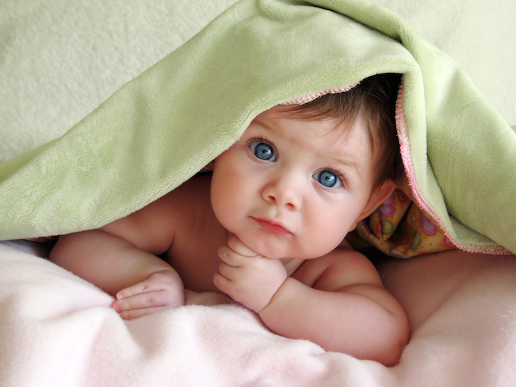 beautiful baby looking out from under blanket